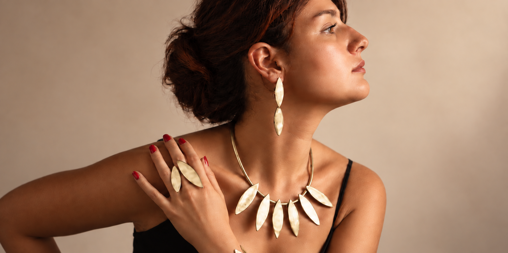 Modella di profilo con collana, orecchini, anello e bracciale dalle forme affusolate